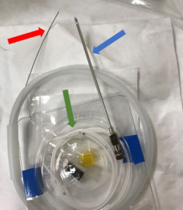 Figure 1 – An opened Integra® HermeticTM Lumbar Catheter Closed Tip kit with straight-ended guidewire (red arrow) exiting the plastic dispenser, spinal needle (blue arrow), and lumbar drain catheter (green arrow) displayed.